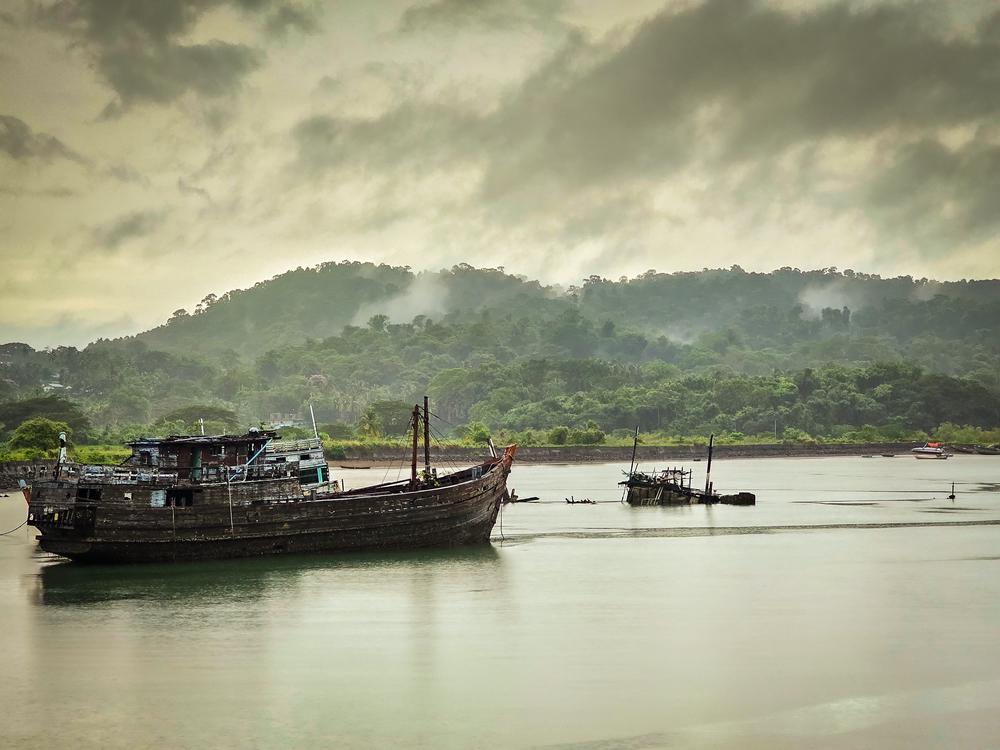 Rusting shipwrecks anchored in the misty waters of Port Blair harbor with lush green hills in the background, Andaman Islands